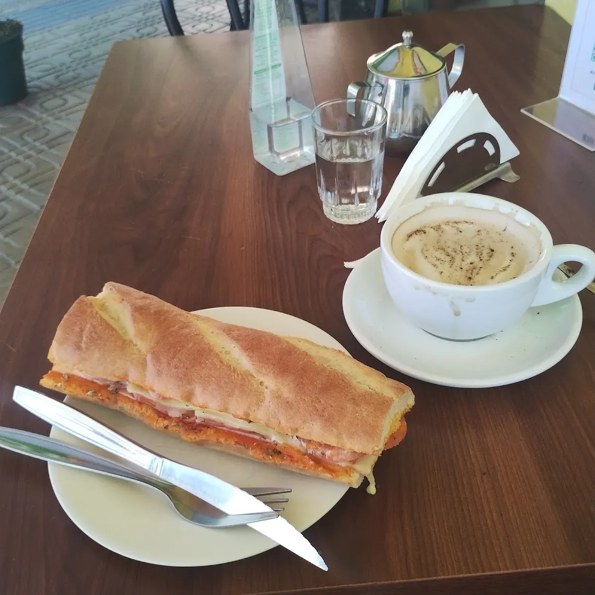 Sándwich de Il Gourmet servido con capuchino sobre servilleta con el logo