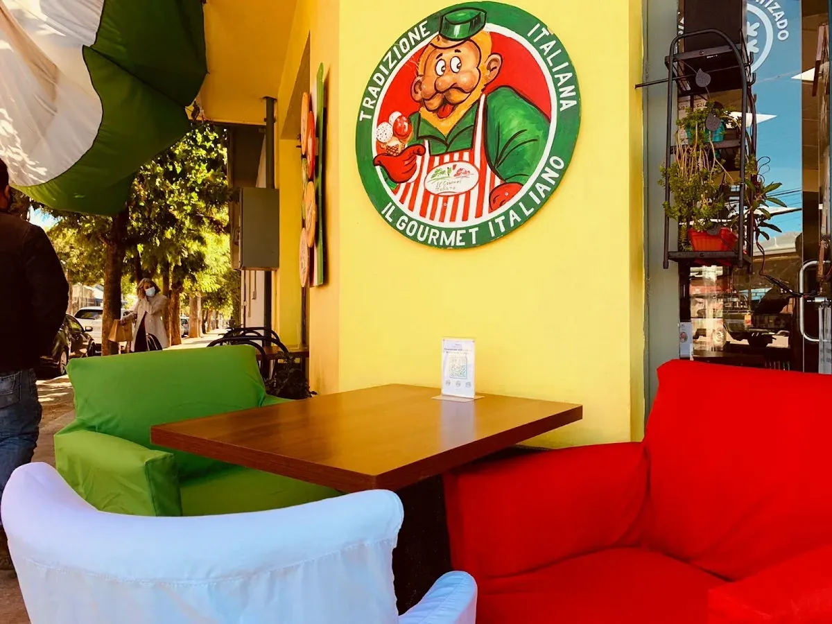 Terraza de Il Gourmet Italiano con sombrillas y el mural amarillo pintado con su logo