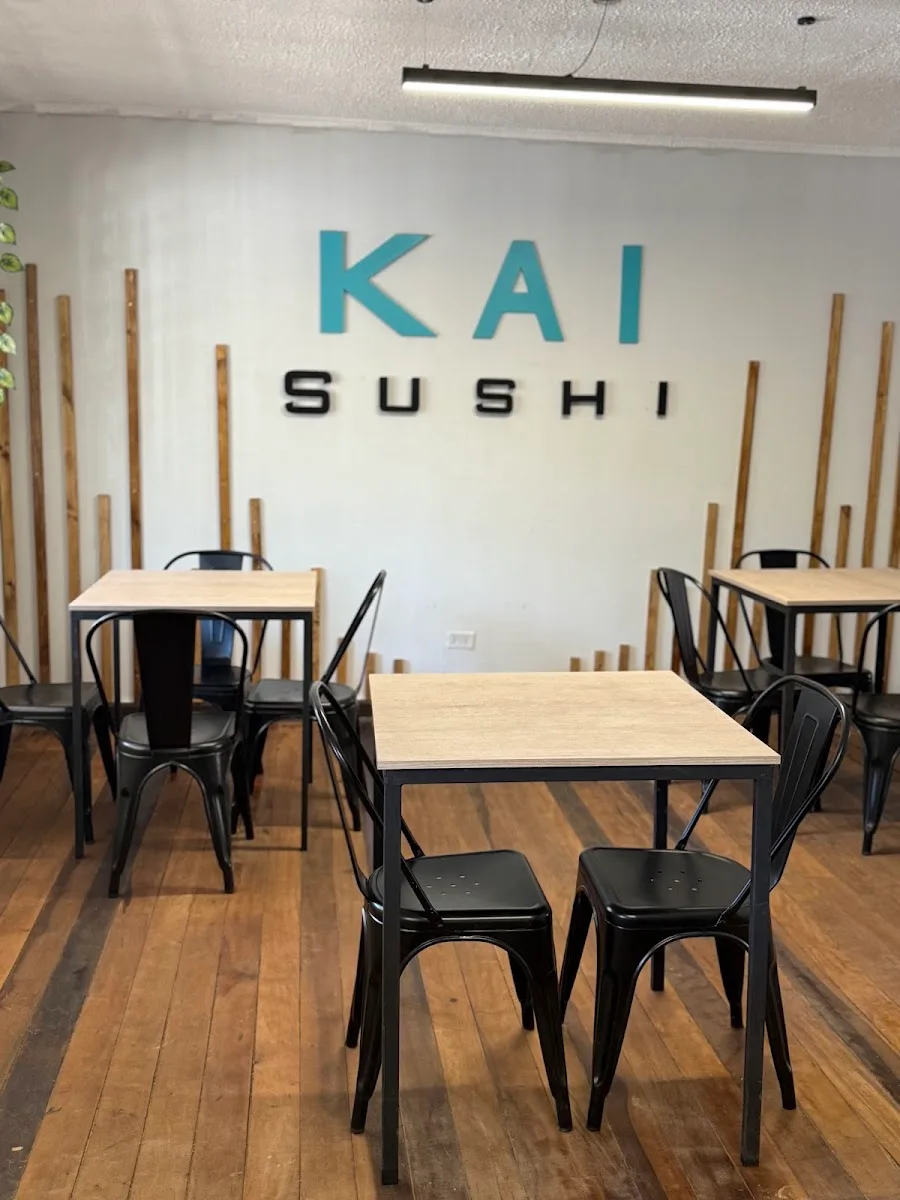 Interior de Kai Sushi con mesas y el logo en el muro