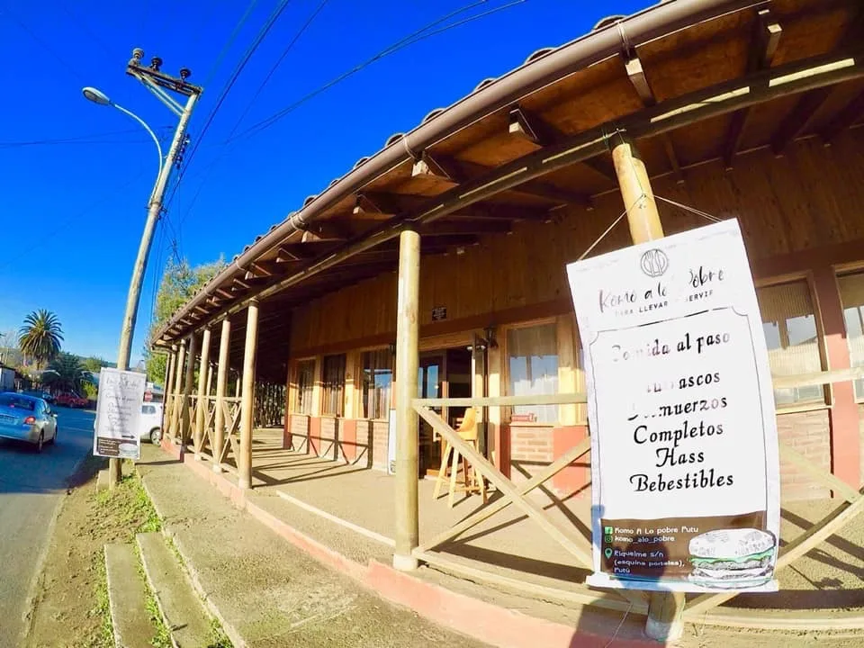 Fachada de Komo a lo Pobre en Putú: casa de madera con letrero colgante de la carta