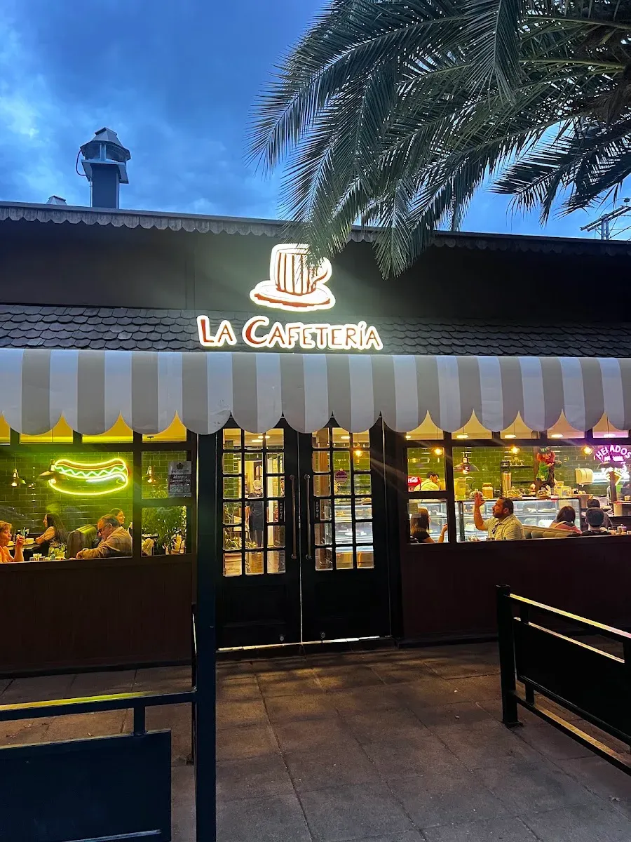 Fachada de La Cafetería de noche, con el letrero de neón encendido