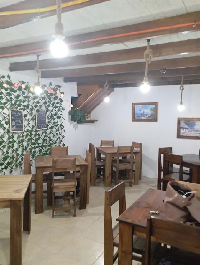Interior de La Picá de Pato Miza: mesas y sillas de madera rústica, ampolletas colgantes y muro de hiedra con pizarras