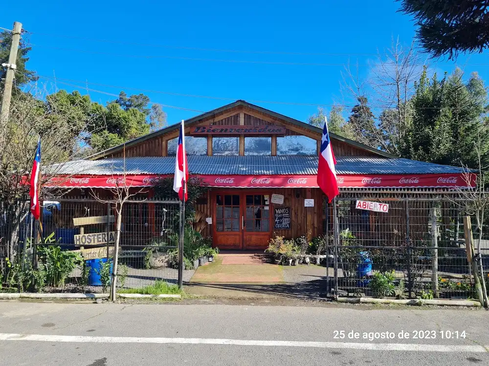 Fachada de madera de Las Puertas del Paraíso con banderas chilenas, toldo y letrero de hostería junto a la Panamericana