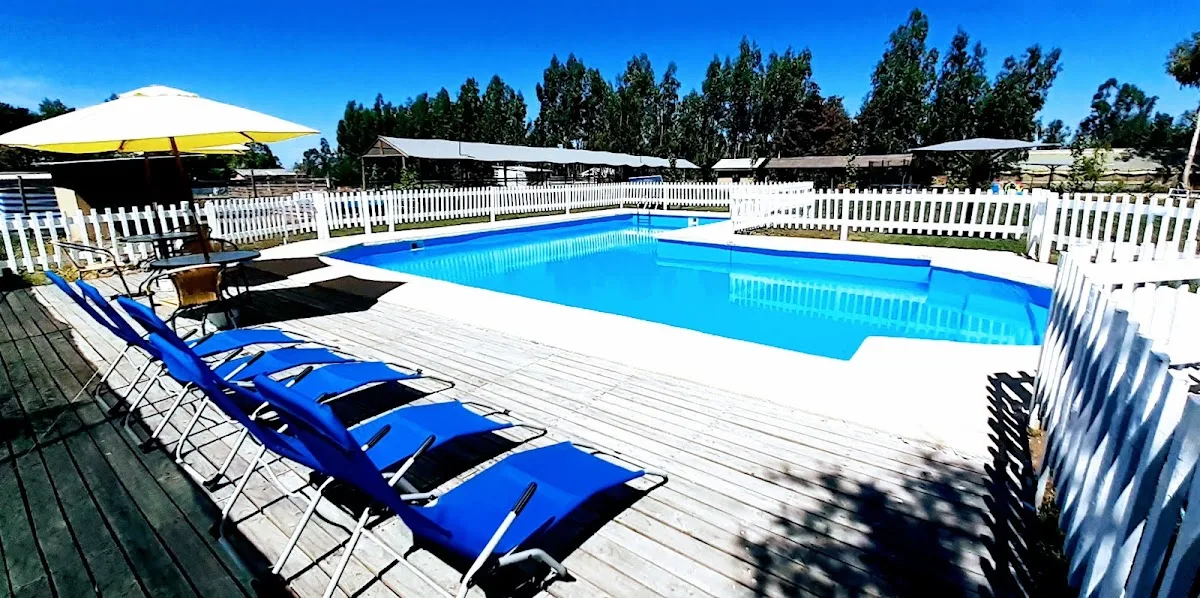 Piscina de Los Treiles: agua celeste rodeada de pasto, reposeras azules y sombrilla
