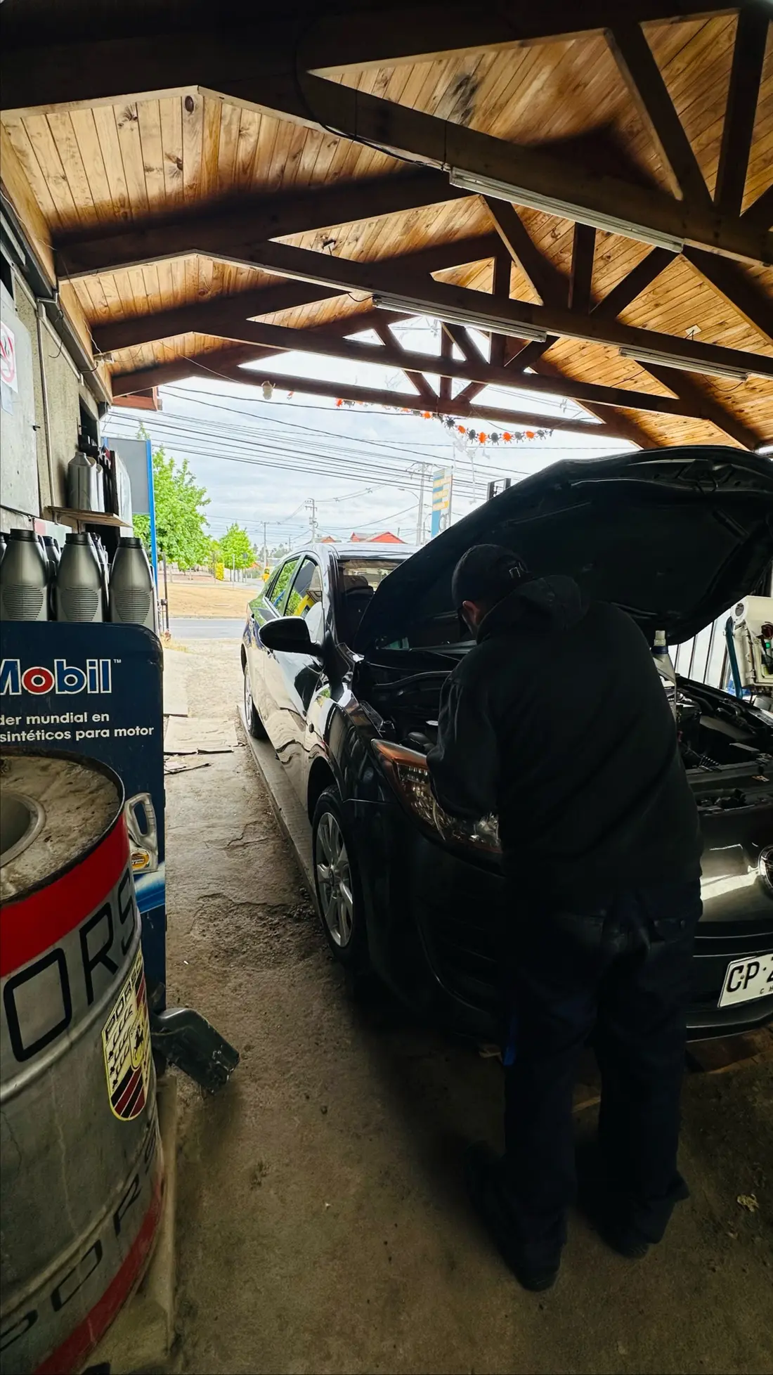 Bahía techada del taller con un auto en mantención y bidones Mobil al costado