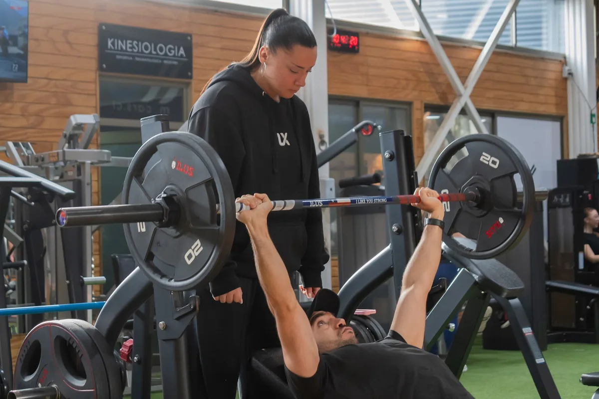 Entrenador de Luxe Gym asistiendo un press de banca con barra olímpica