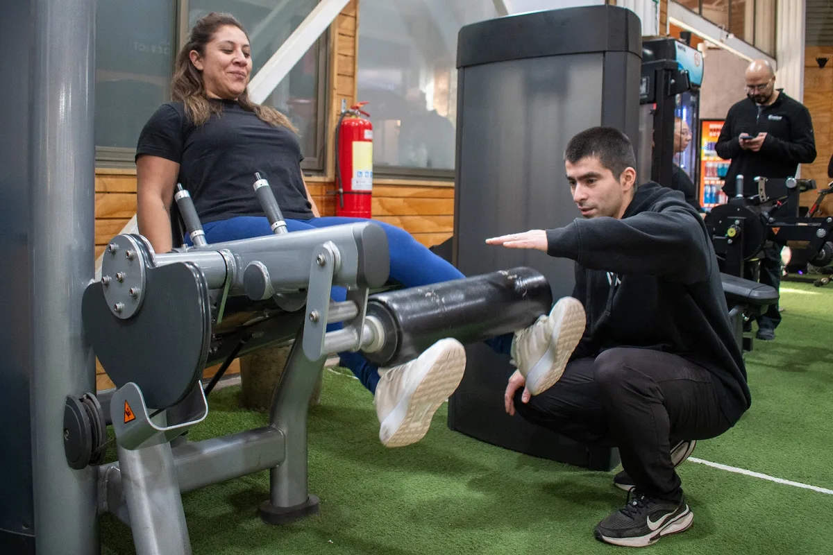 Alumna entrenando en prensa de piernas con asistencia del staff de Luxe Gym
