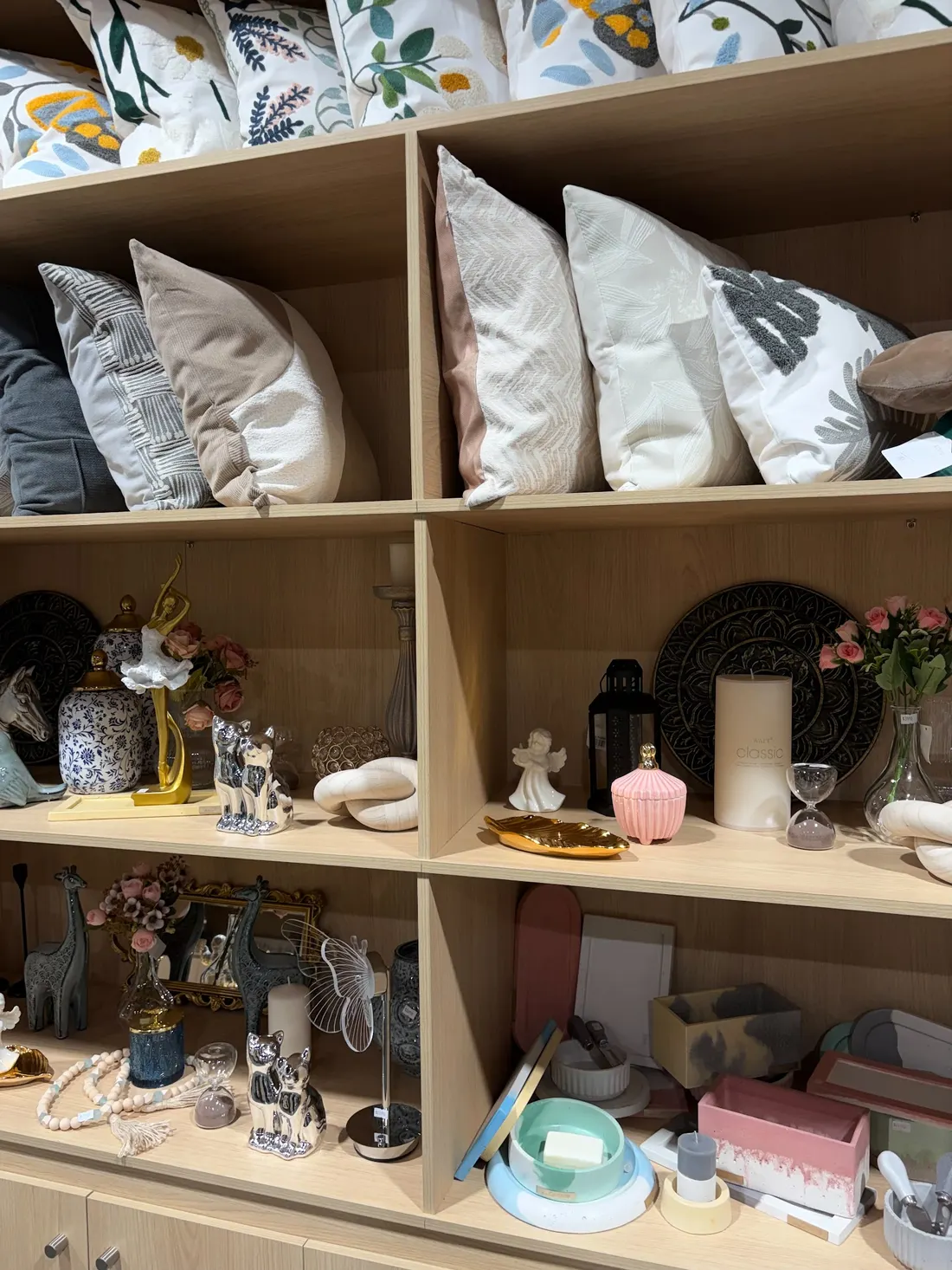Repisas de la tienda con cojines bordados, figuras de porcelana, velas y jarrones