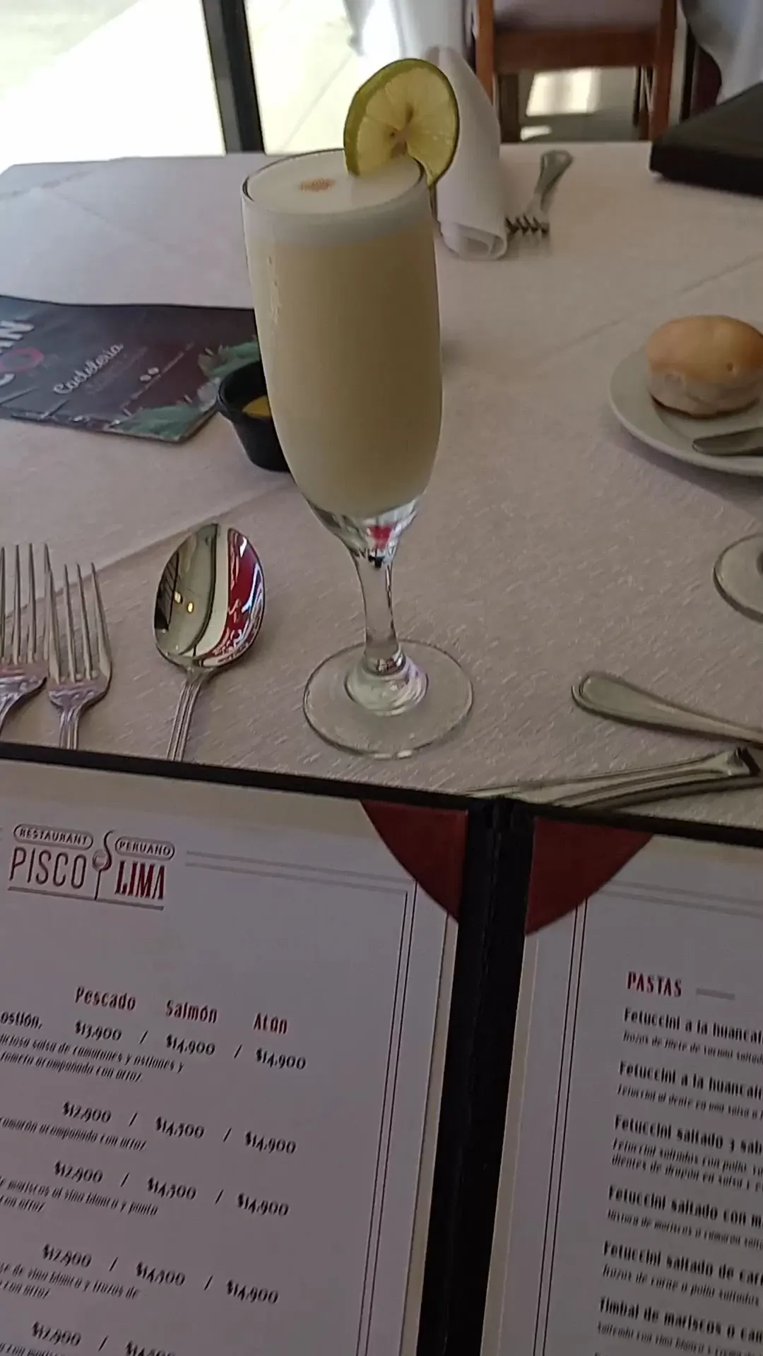 Pisco sour servido en la mesa con cubertería de la casa