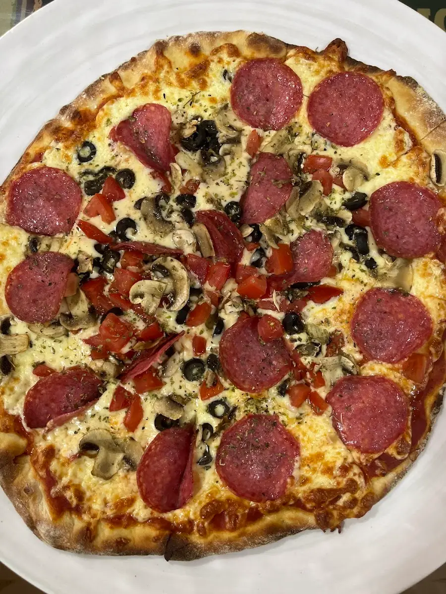 Pizza de pepperoni con aceitunas negras y orégano de Pizzería la Toscana, recién salida del horno