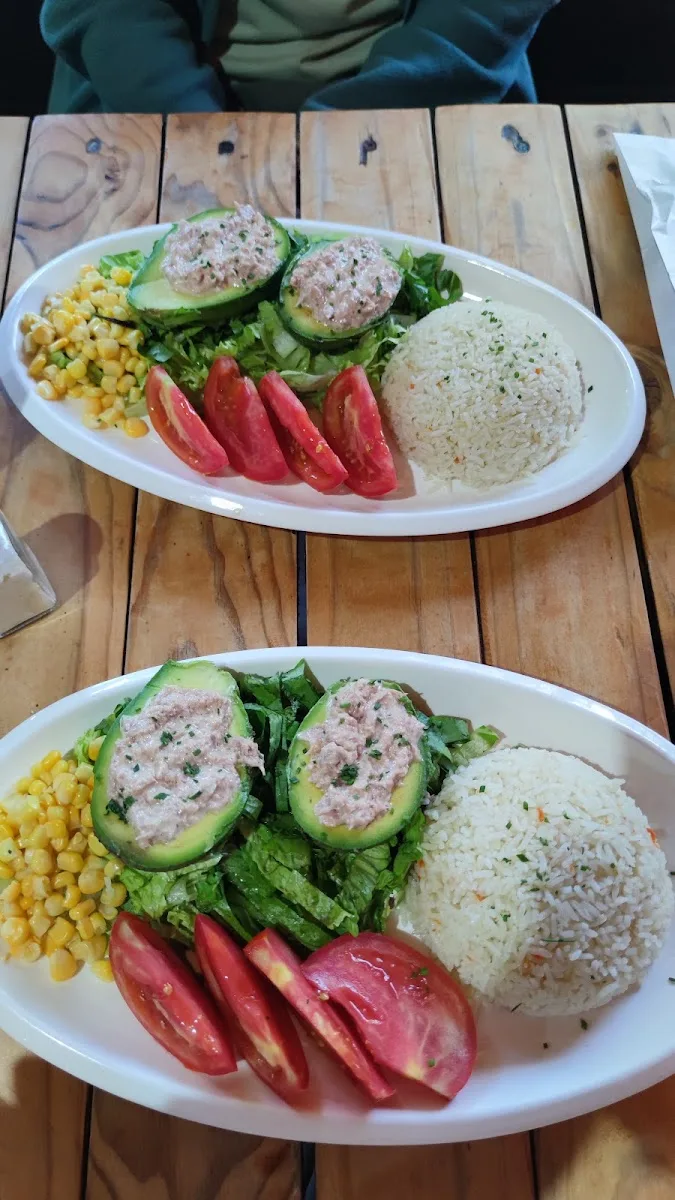 Dos paltas rellenas con arroz, tomate y choclo servidas en mesa de madera