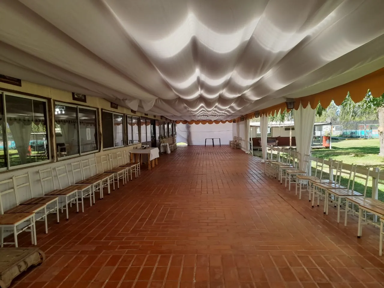 Corredor techado con piso de ladrillo, cortinas blancas y vista al jardín
