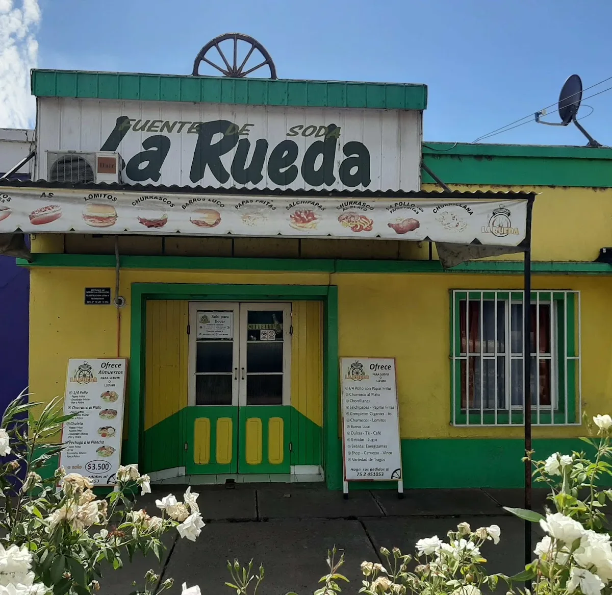 Fachada de la Fuente de Soda La Rueda con la rueda de carreta en el techo, toldo verde y banderines de colores