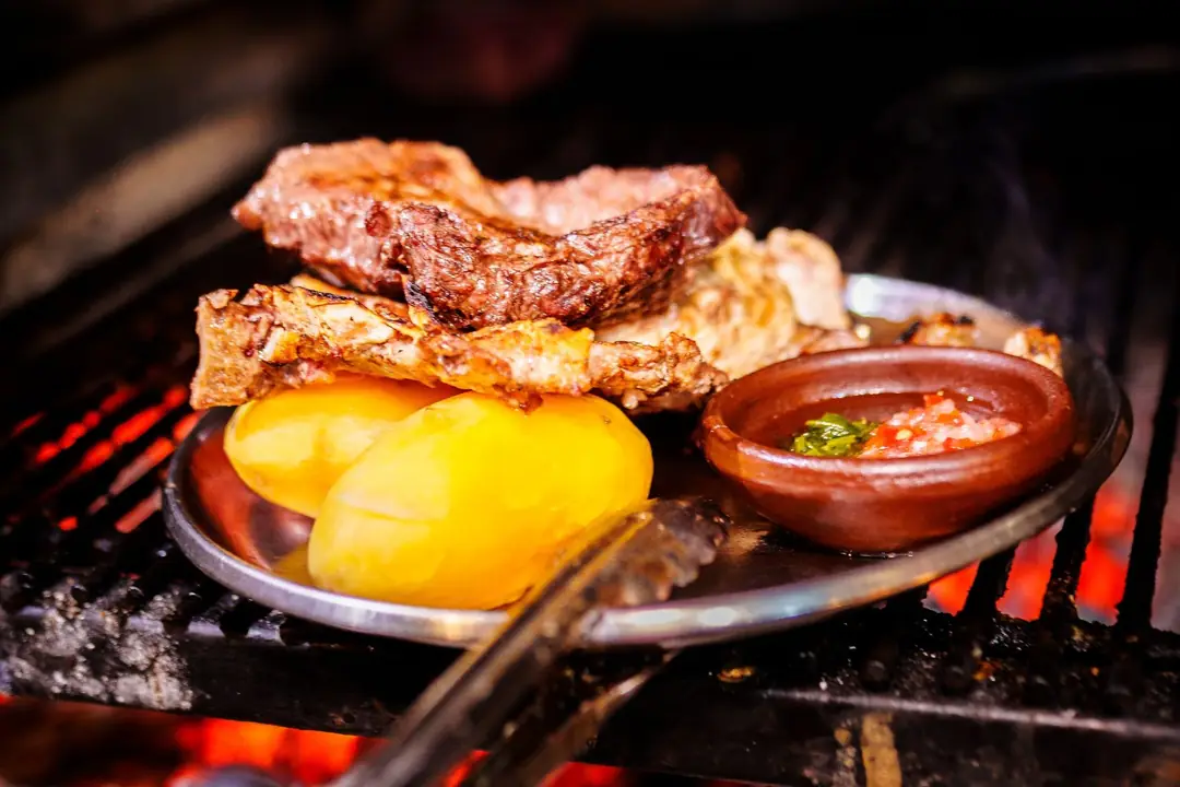 Parrillada con papas y pebre en plato de greda sobre las brasas