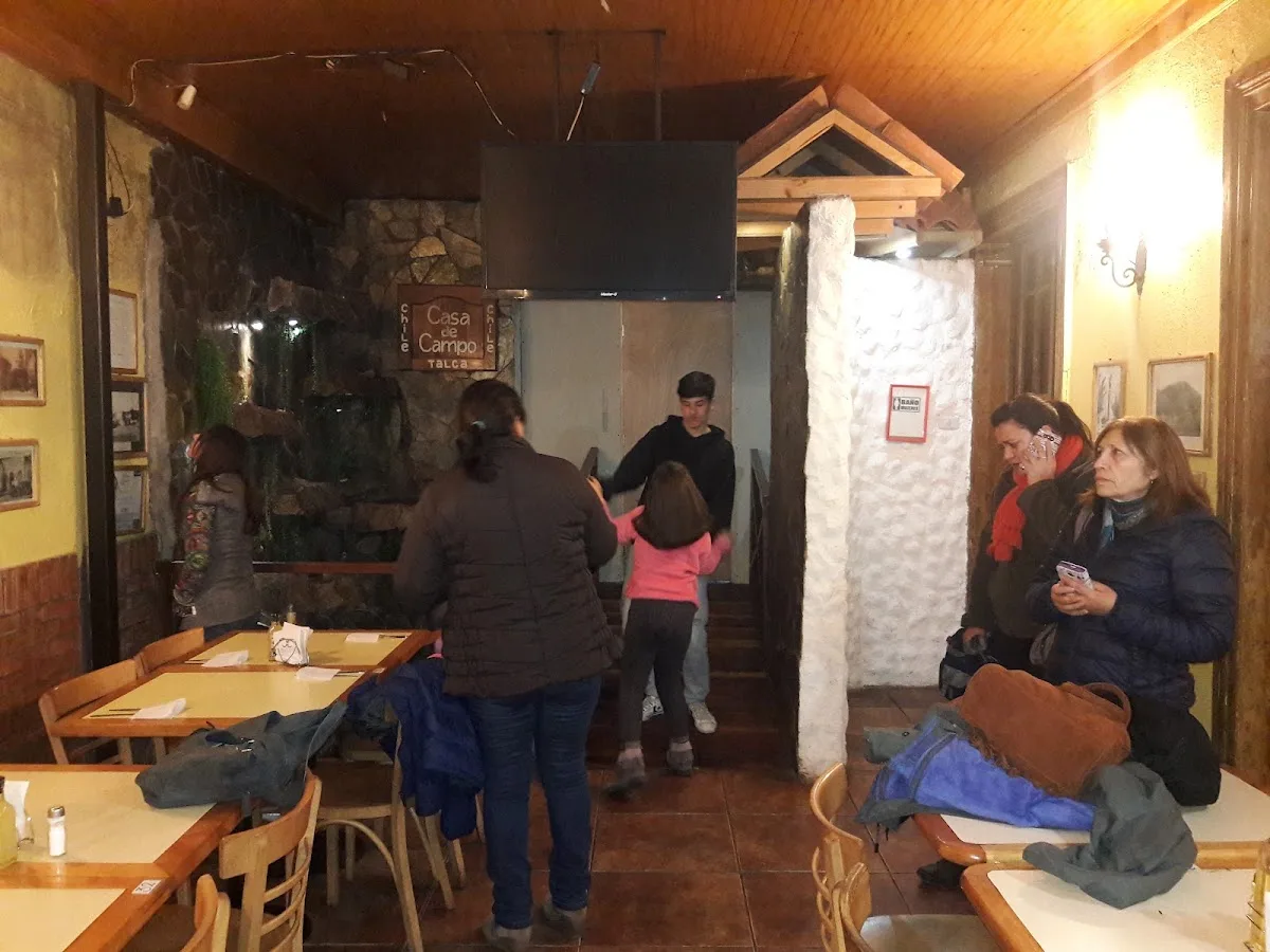 Salón interior de Casa de Campo con muro de piedra y mesas