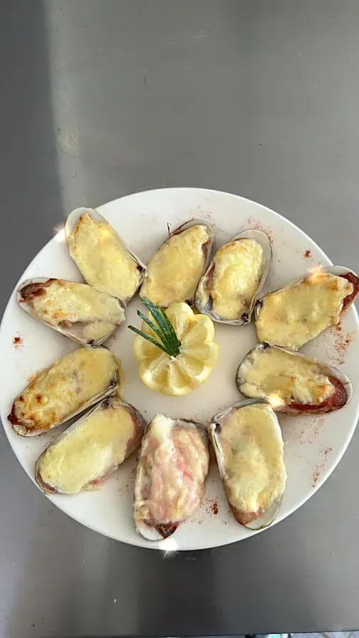 Machas a la parmesana gratinadas, servidas en círculo sobre plato blanco con limón