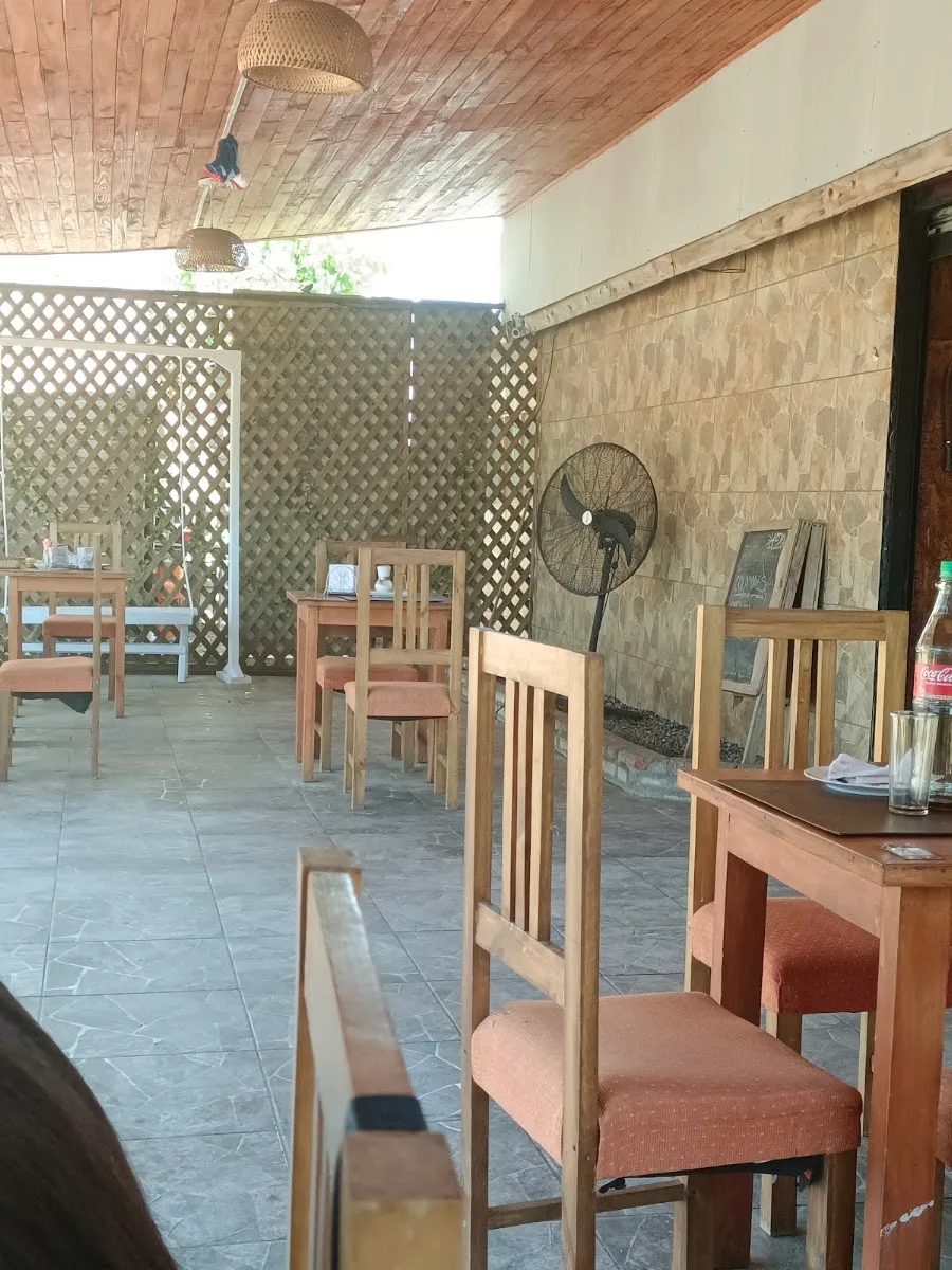 Terraza del comedor con mesas de madera, sillas con cojín y lámparas de mimbre bajo el techo