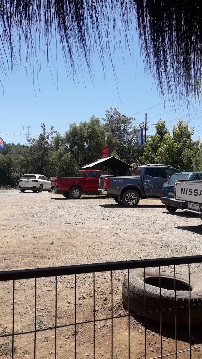 Estacionamiento amplio frente al restaurante con banderas chilenas y árboles al fondo