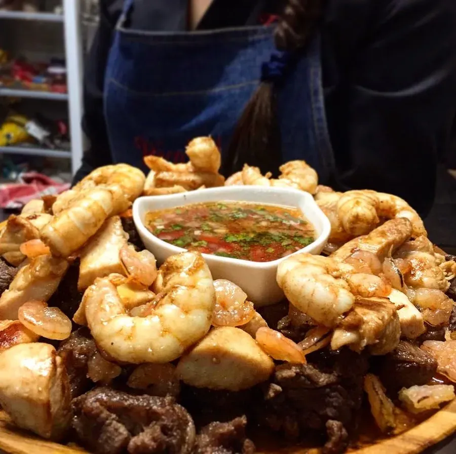 Tabla de parrillada con camarones y carne alrededor de una salsa fresca
