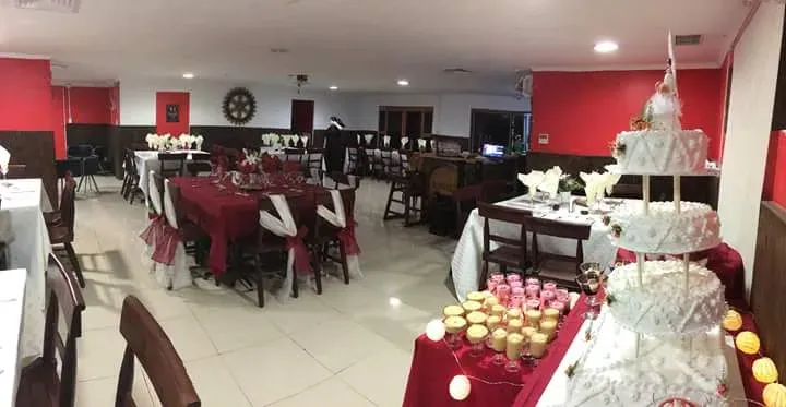 Salón de eventos de Rico's preparado para un matrimonio: mesas con mantel burdeo y torta de varios pisos