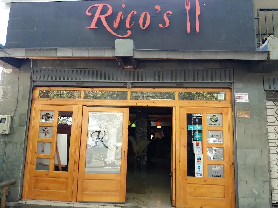 Fachada de Rico's Restaurant: muro oscuro, letrero rojo con el nombre y puertas de madera