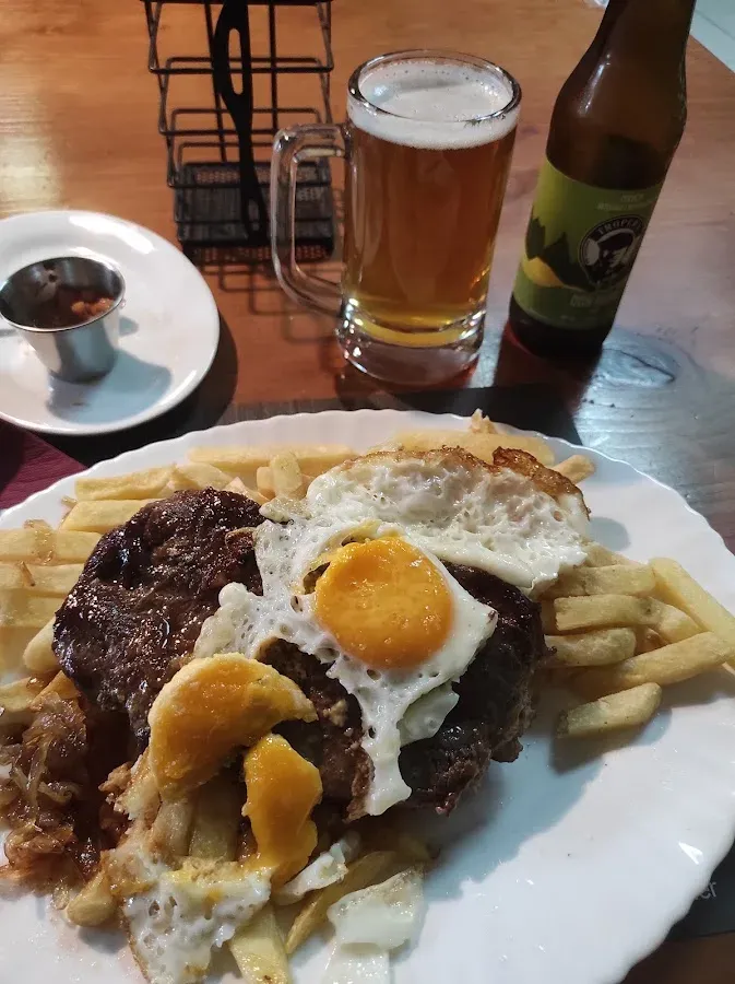 Lomo a lo pobre con huevo frito y papas, junto a un schop de cerveza y una botella artesanal