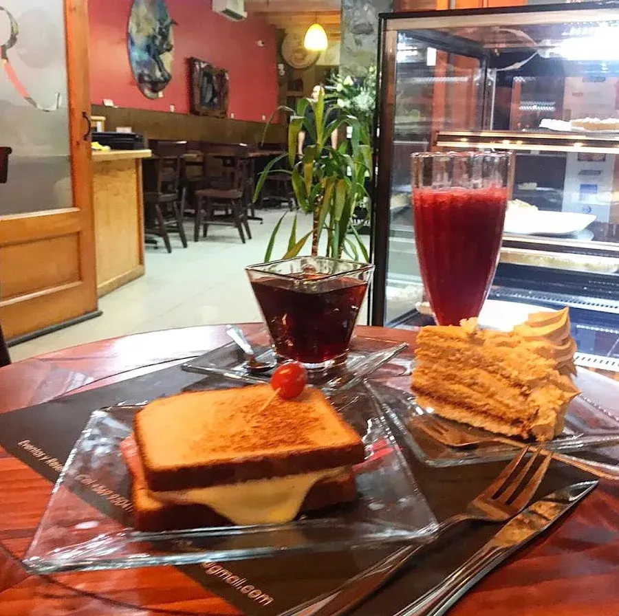 Mesa con trozo de torta, lámina de leche y jugo de frambuesa junto a la vitrina de postres