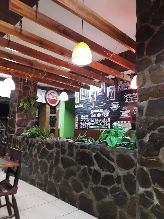 Interior de Rico's: muro de piedra, vigas de madera, lámparas y la pizarra con la carta de cafetería