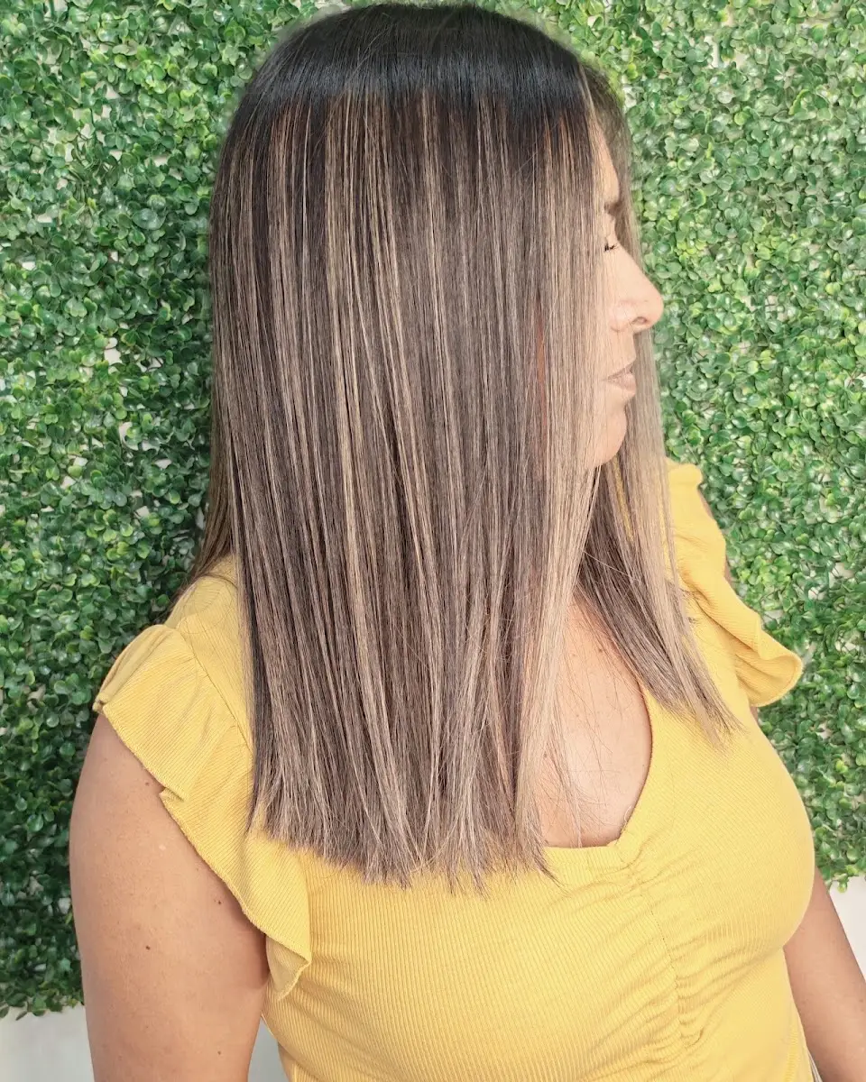 Cliente del salón con cabello rubio lacio en perfil, junto al muro verde