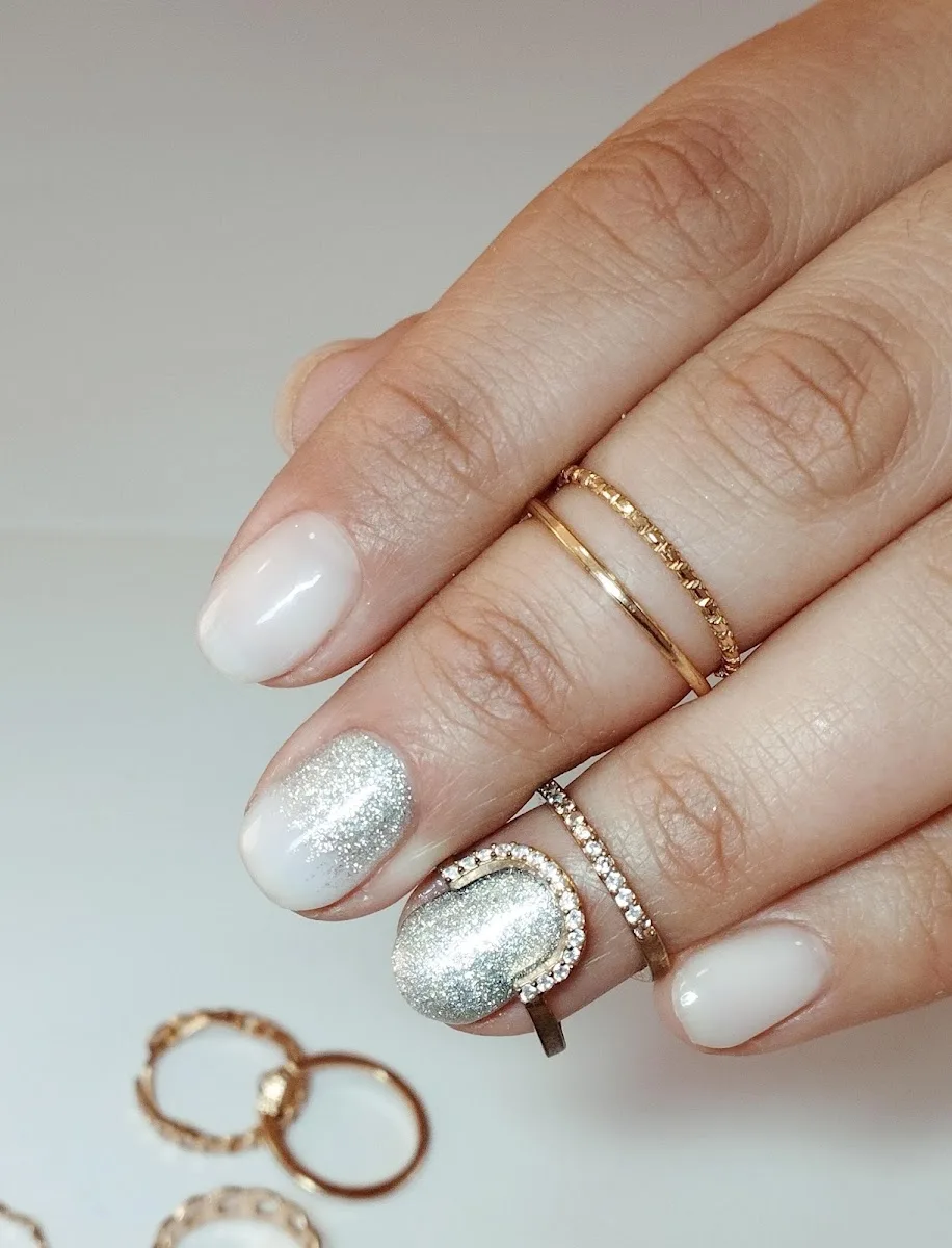 Manicure del salón: uñas en blanco con glitter plateado y anillos dorados