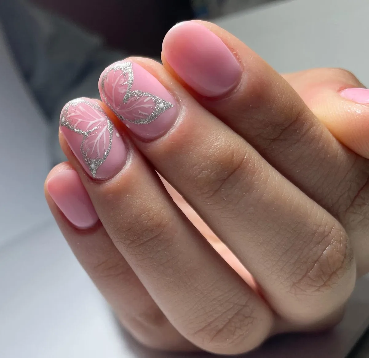 Uñas rosadas con diseño de mariposas y glitter hechas en el salón