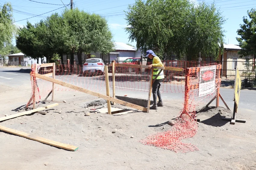 Zanja abierta en la vereda con trabajador instalando tubería, obra sanitaria en Huépil