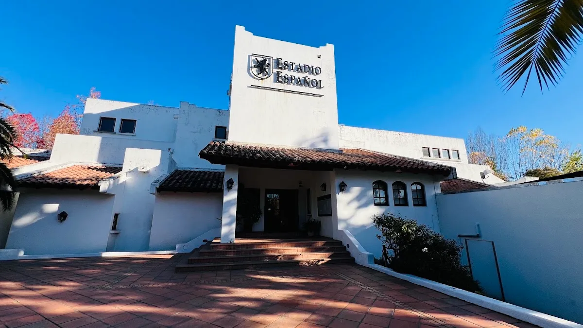 Fachada blanca estilo andaluz del Estadio Español de Linares, con tejas, palmeras y el escudo negro del club