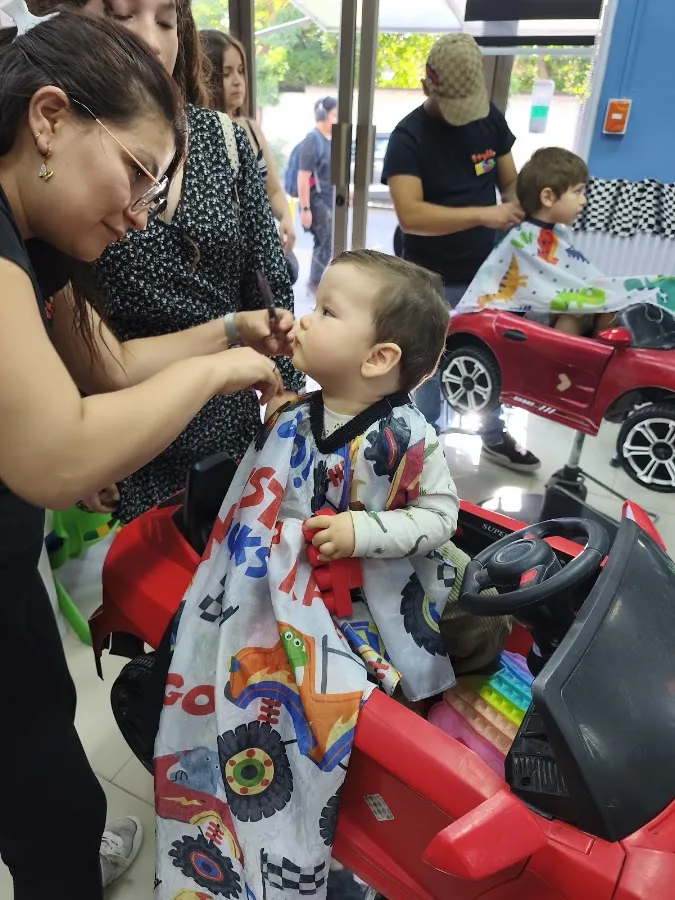 Niño sentado en una silla-auto roja mientras le cortan el pelo