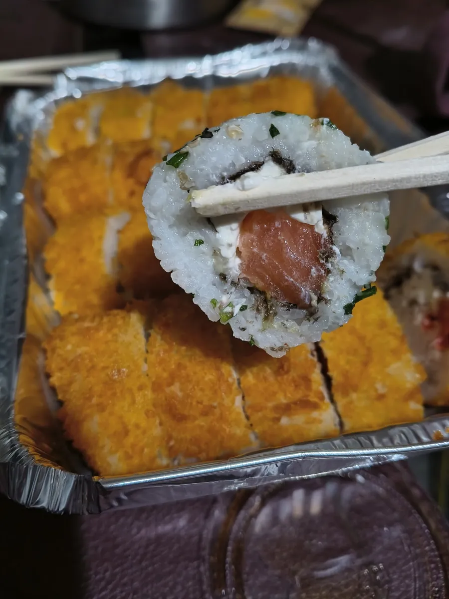 Roll de salmón sostenido con palillos sobre la mesa de acero del local