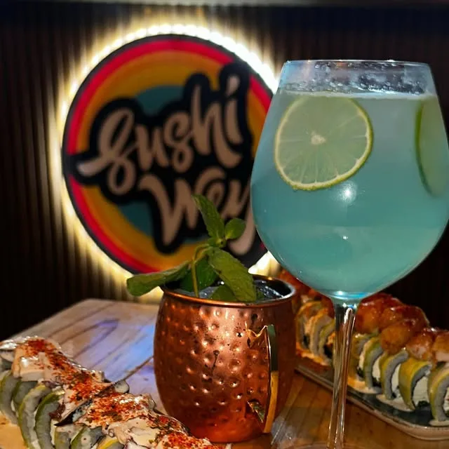 Mesa de Sushi Wey con rolls, cóctel celeste y su letrero de neón encendido