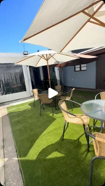 Patio exterior con pasto sintético, mesas y paraguas blancos