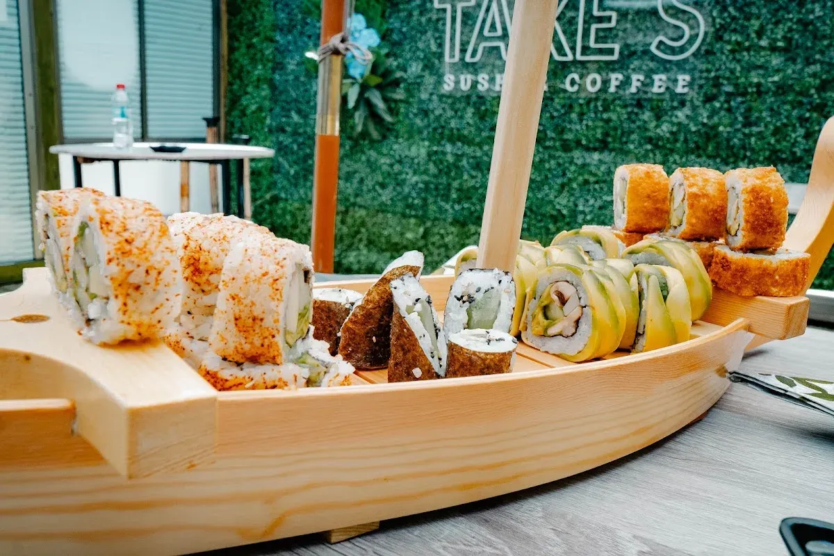 Tabla de sushi con rolls variados frente al muro verde de Take’s