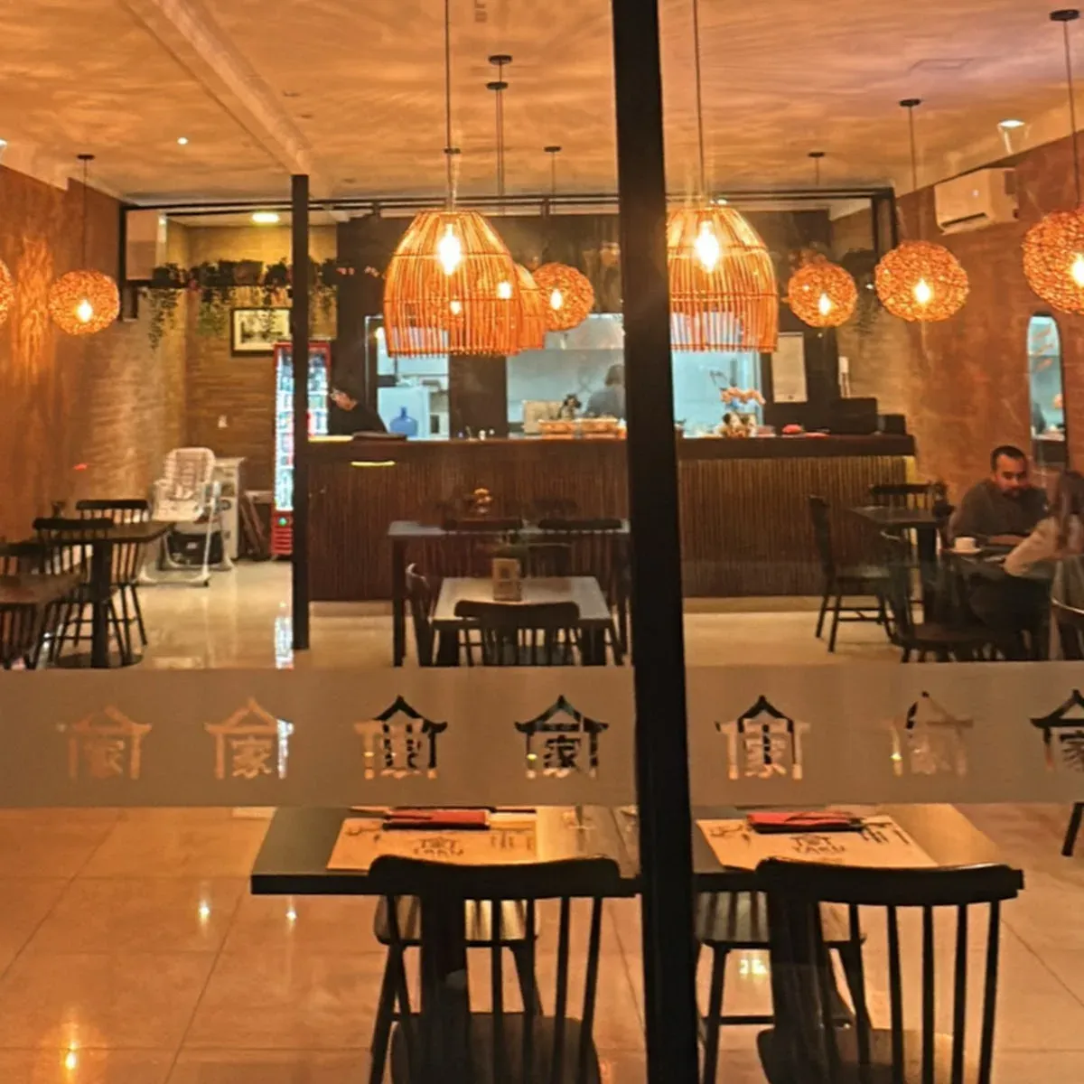 Salón de TAKU NIKKEI con lámparas cálidas y el logo de la casa en el vidrio, Talca