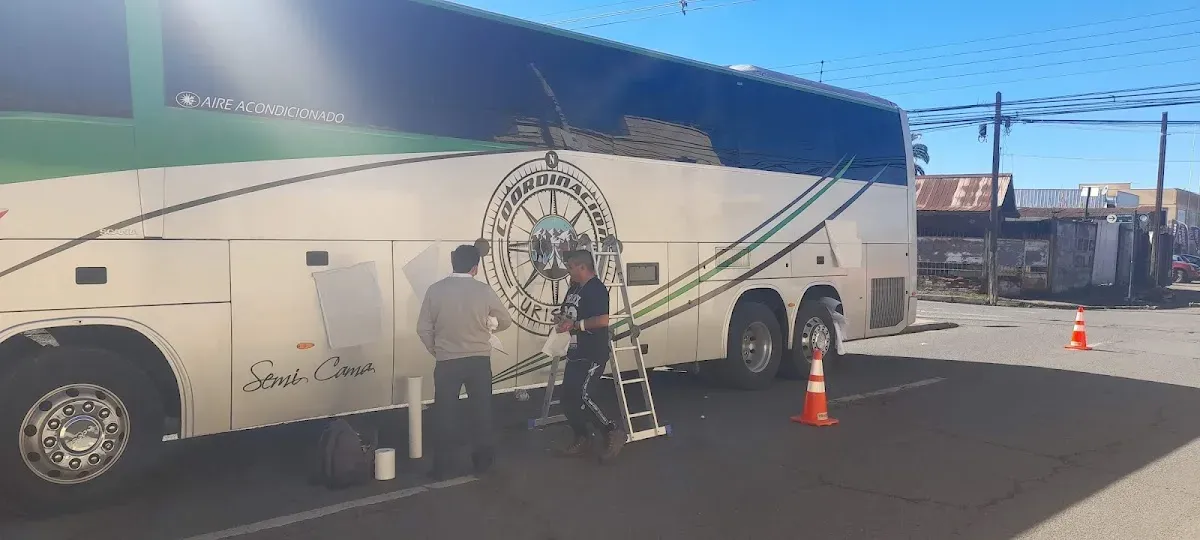 Dos personas instalando un vinilo gigante sobre la carrocería de un bus